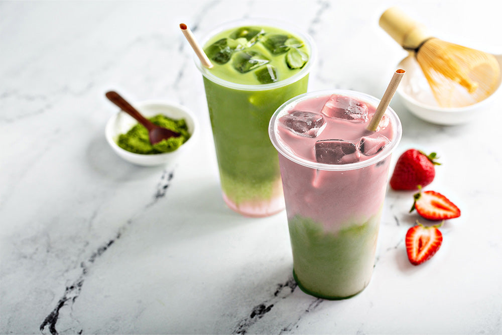 Matcha powder, iced matcha latte, strawberry matcha iced latte, strawberries, all on a marble countertop