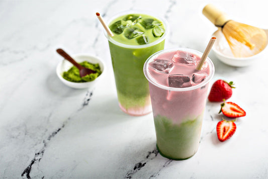 Matcha powder, iced matcha latte, strawberry matcha iced latte, strawberries, all on a marble countertop