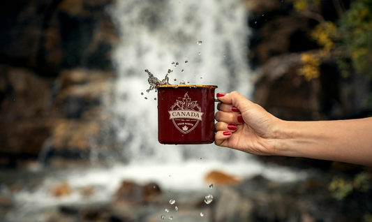 Woman's hand holding a Canada mug in front of a waterfall