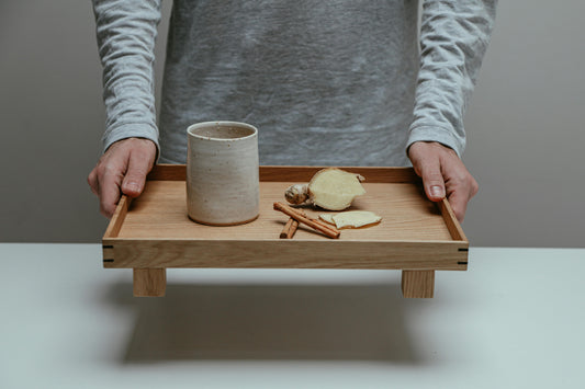 Person Holding a Wooden Serving Tray with a Cup and Herbs