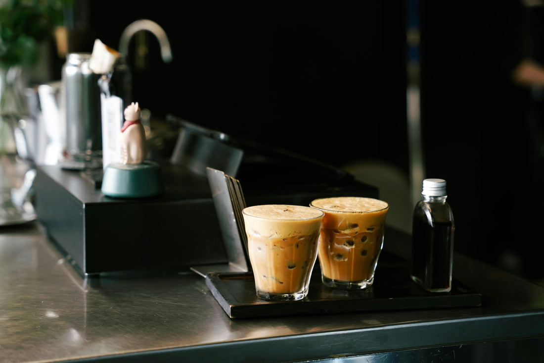 Two London Fog lattes in glass cups on a counter at a cafe with vanilla extract beside them