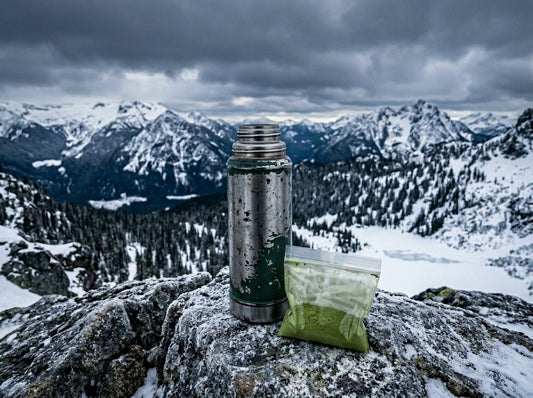 Thermos and a small bag of tea powder on a rocky ledge with a snowy mountain wilderness view behind
