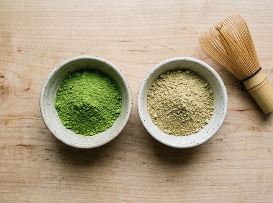 Two ceramic bowls of tea powder side by side on a wooden surface, one plain green matcha and one vanilla matcha tea powder