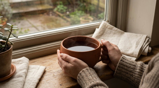 Hands wrapped around a ceramic mug of rooibos tea at a morning window