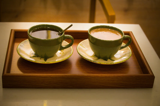 A cup of tea with a spoon, beside a cup of coffee. Both in green teacups on saucers