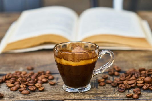 Espresso in a glass cup with coffee beans, and a book in the background