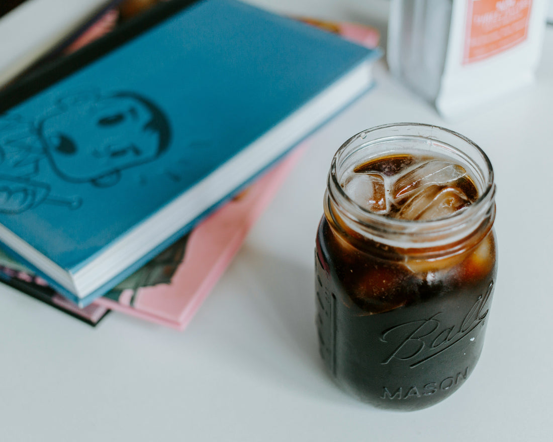 Cold brew coffee in a mason jar with ice, and notebooks in the background and a bag of Miscela D'Oro Coffee