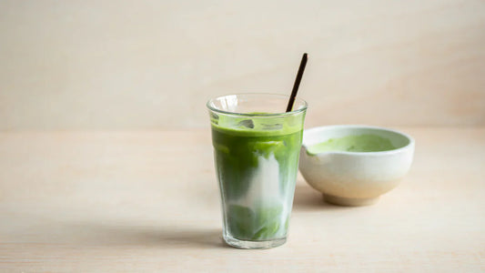 Matcha iced latte in a glass with a spoon inside, beside a bowl of matcha powder
